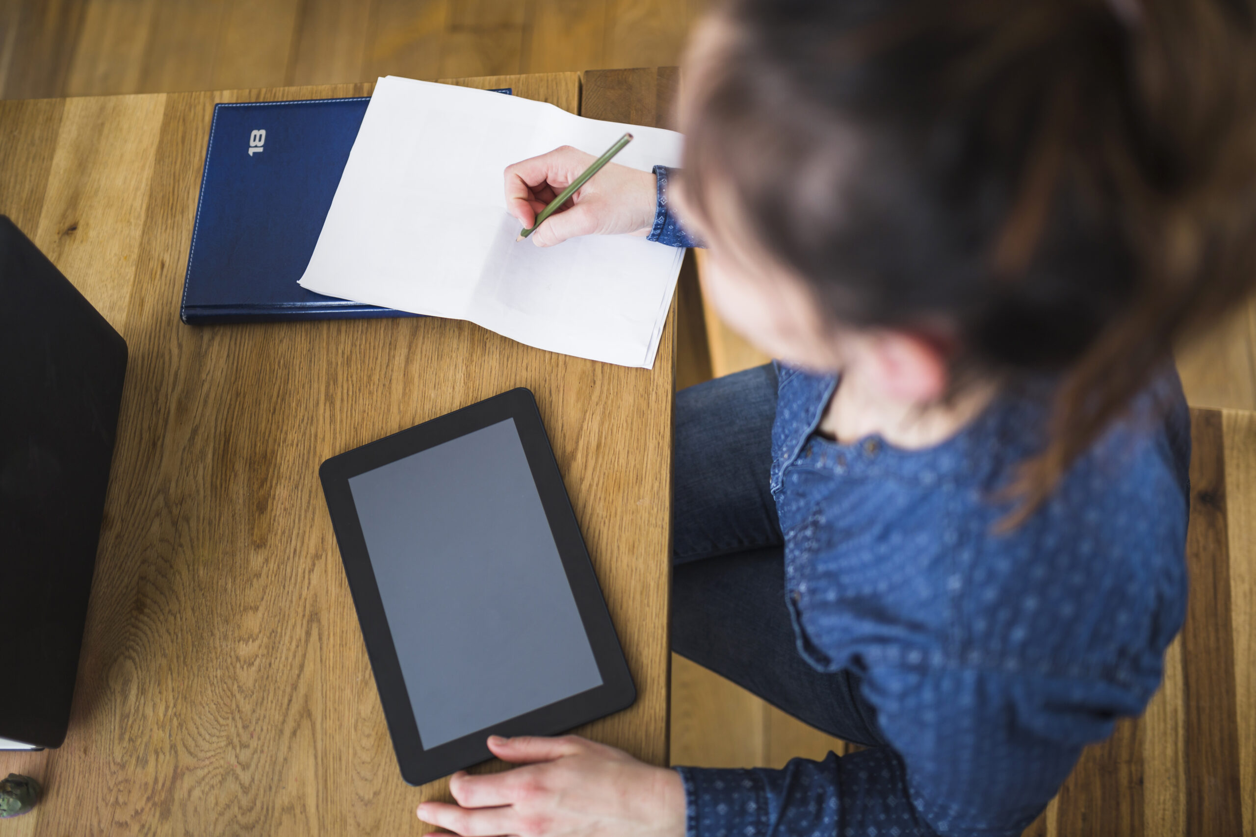 woman writing notes paper with digital tablet wooden desk